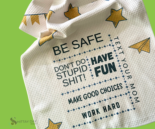 White waffle weave kitchen towel with funny college advice, yellow stars and paper airplanes. Advice text "Be Safe, Have Fun, Don't do stupid shit, Text your Mom, Make good choices, work hard". On a green background.