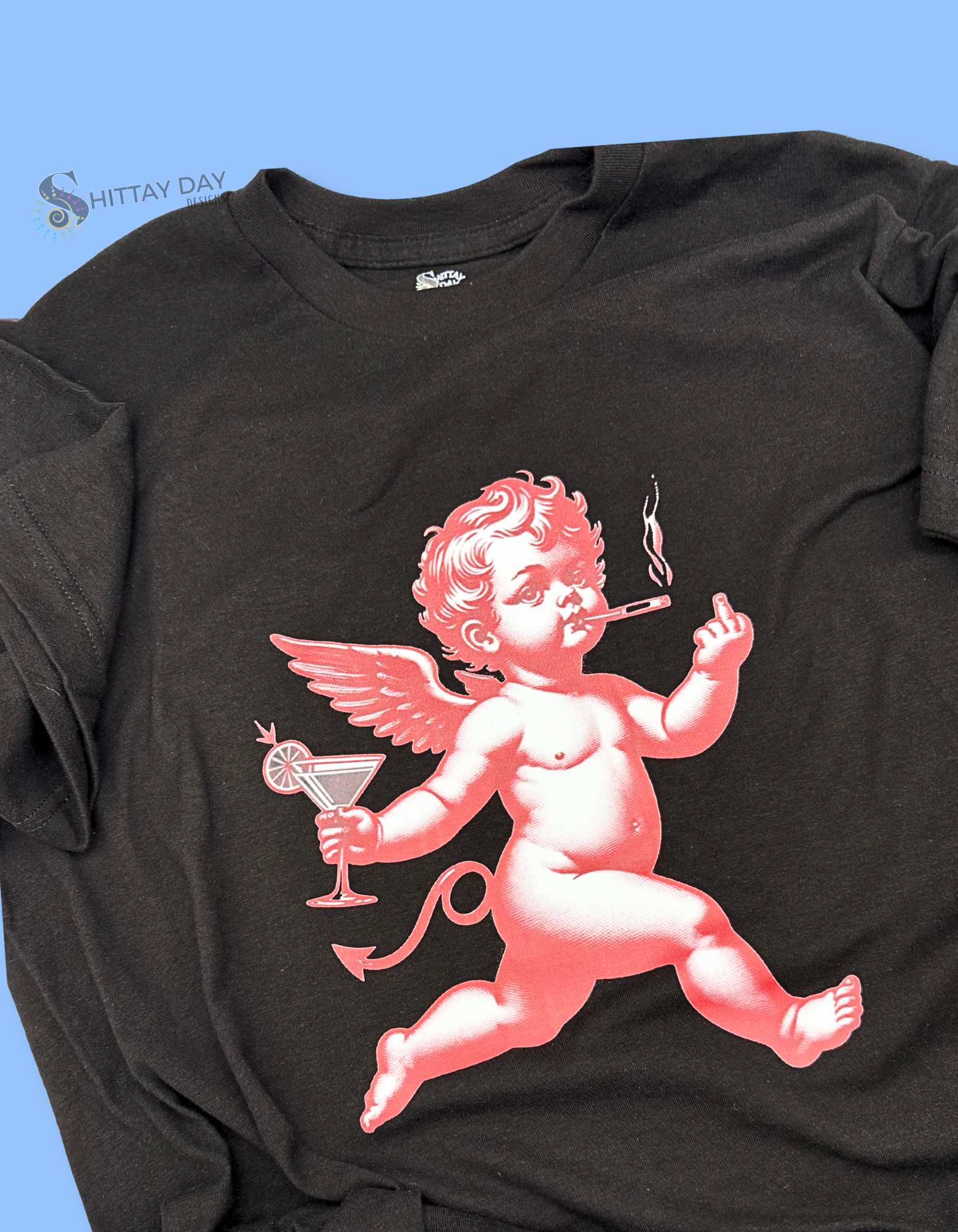 Black t-shirt with a red cherub smoking a cigarette, holding a martini glass, and flashing a middle finger design on a blue background.