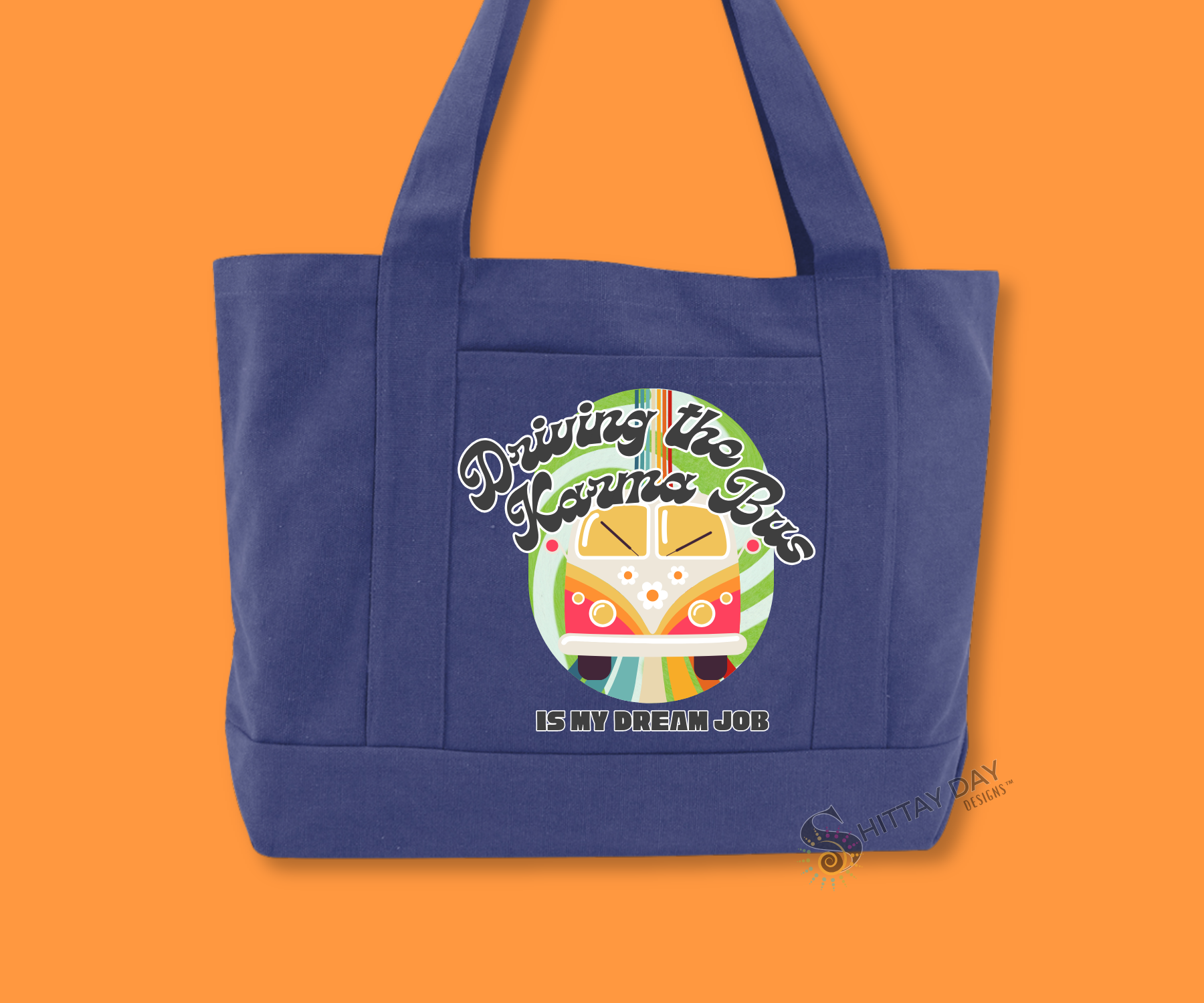 A blue pocket front tote bag with colorful graphic of a retro bus and colorful swirl background with the text "driving the karma bus is my dream job". The picture background is orange.