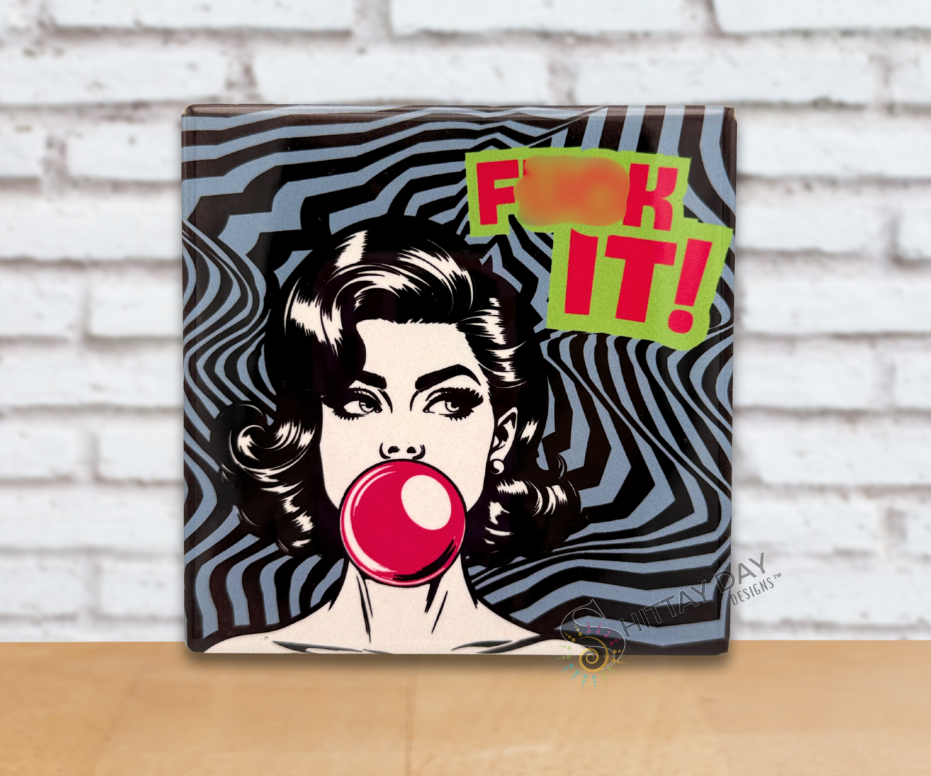 Pop art-style ceramic coaster with a woman blowing a bubble gum bubble and a bold exclamation reading 'F*ck It!' text on an abstract grey and black background.