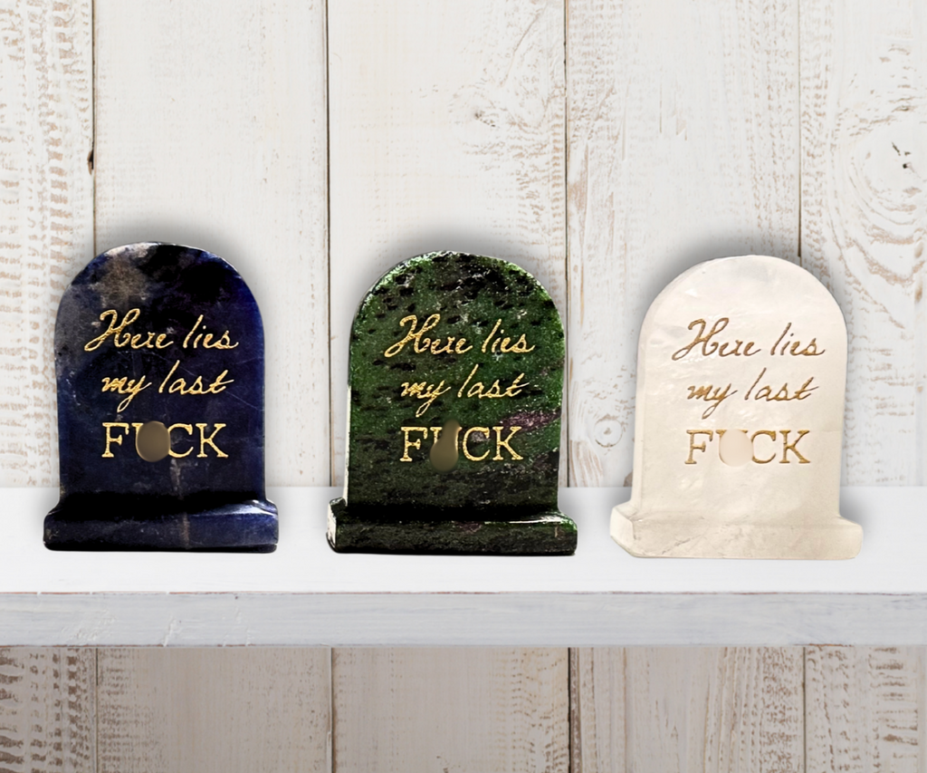 Close-up of 3 natural crystal carved tombstones reading “Here lies my last F*CK.”
