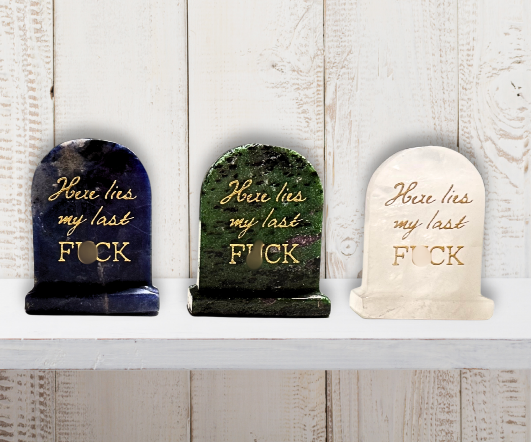 Close-up of 3 natural crystal carved tombstones reading “Here lies my last F*CK.”
