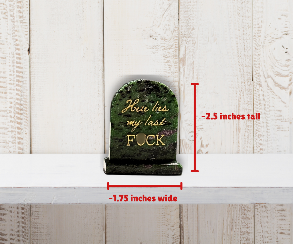 Natural crystal “Here lies my last F*CK” tombstone shown beside a size reference, approximately 6 cm tall.
