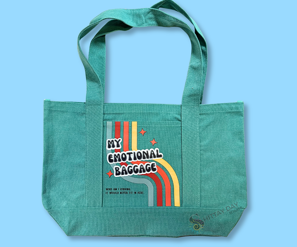 Teal pocket tote with design text 'My Emotional Baggage, who am I kidding, it would never fit',  a multicolor retro stripe, and orange starbursts. Merchandised on an light blue background.