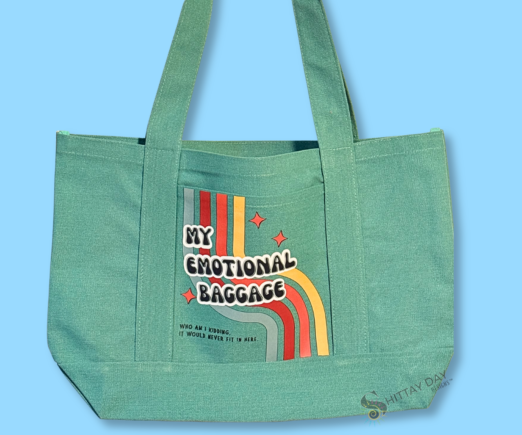 Teal pocket tote with design text 'My Emotional Baggage, who am I kidding, it would never fit',  a multicolor retro stripe, and orange starbursts. Merchandised on an light blue background.