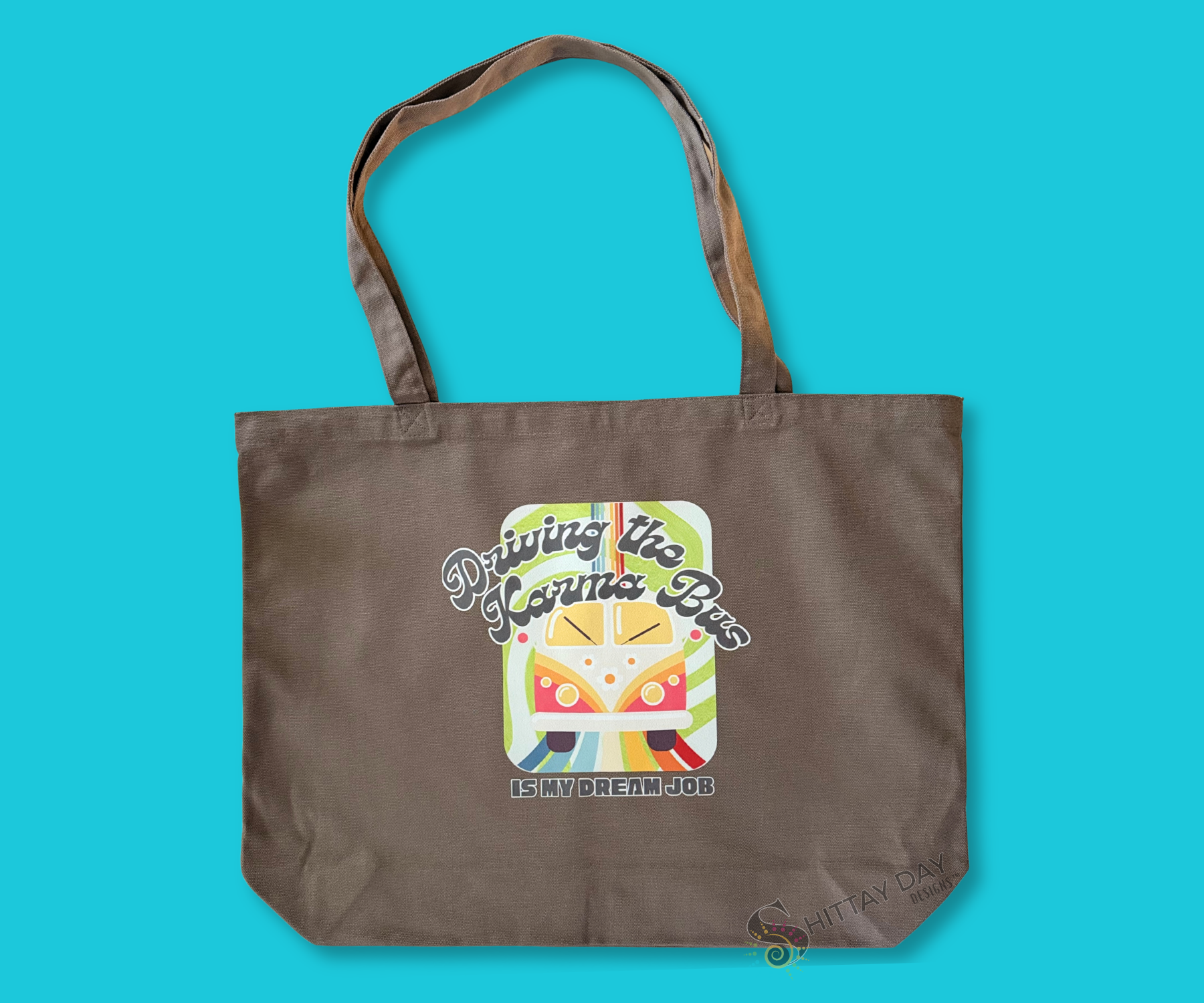 Decorative gray brown tote bag with a colorful graphic of a retro bus, colorful swirl pattern design, and text merchandised on a blue background