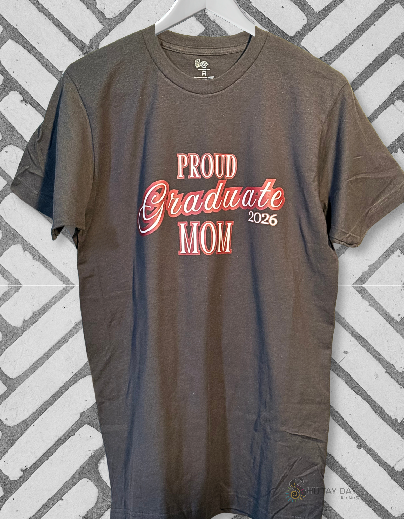 Gray color hanging  tshirt with a close up of the design; 'Proud Graduate Dad 2026'  maroon outlined white l text. Merchandised on a blue background.
