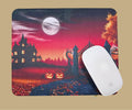 A mouse pad with a Halloween-themed illustration, featuring a haunted house, full moon, pumpkins, and a gate, shown with a white  mouse on top.
