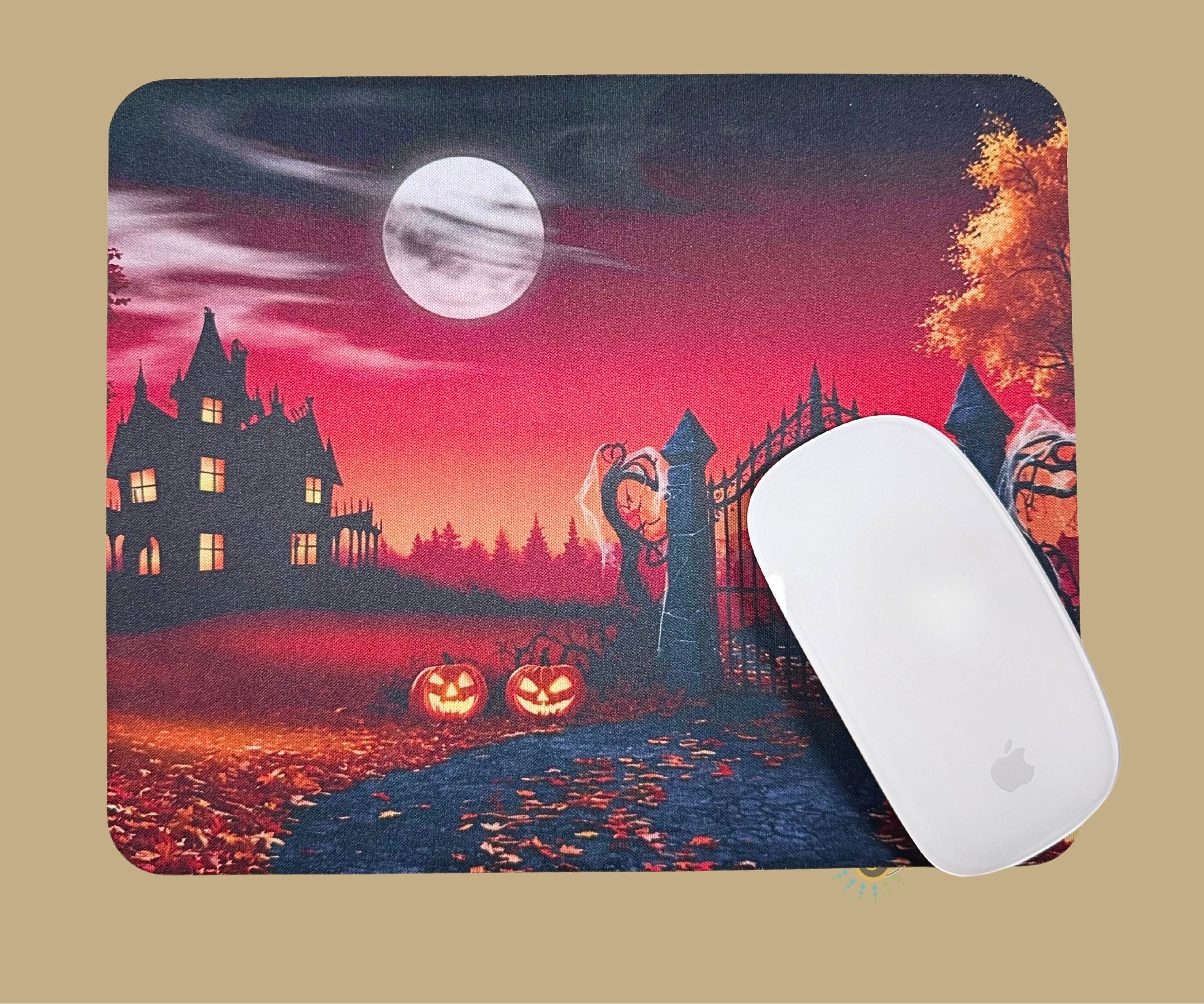 A mouse pad with a Halloween-themed illustration, featuring a haunted house, full moon, pumpkins, and a gate, shown with a white  mouse on top.