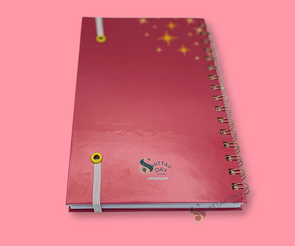 Back cover of the What? Like it's hard? grad wire bound notebook with a pink gradient background with yellow stars and small brand logo. featured on a pink background