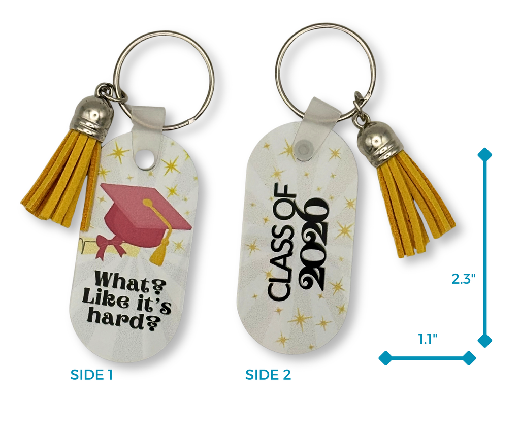 Graduation-themed oval shaped keychain with "What? Like it's Hard? text and a pink grad cap, degree rolled with pink ribbon, and yellow starbursts on side 1 image and "Class of 2026" with yellow starbursts on side 2 image. dimensions shown as 2.3" X 1.1". The keychain also has a yellow tassel. Image is on a white background.