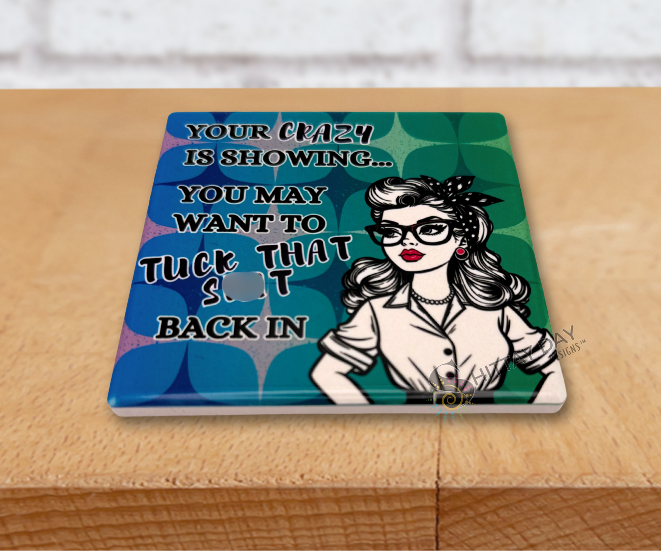 Retro vibe ceramic coaster upright with a woman's illustration and humorous text reading 'Your Crazy Is Showing, You May Want To Tuck That Shit Back in" on a blue and green patterned background.