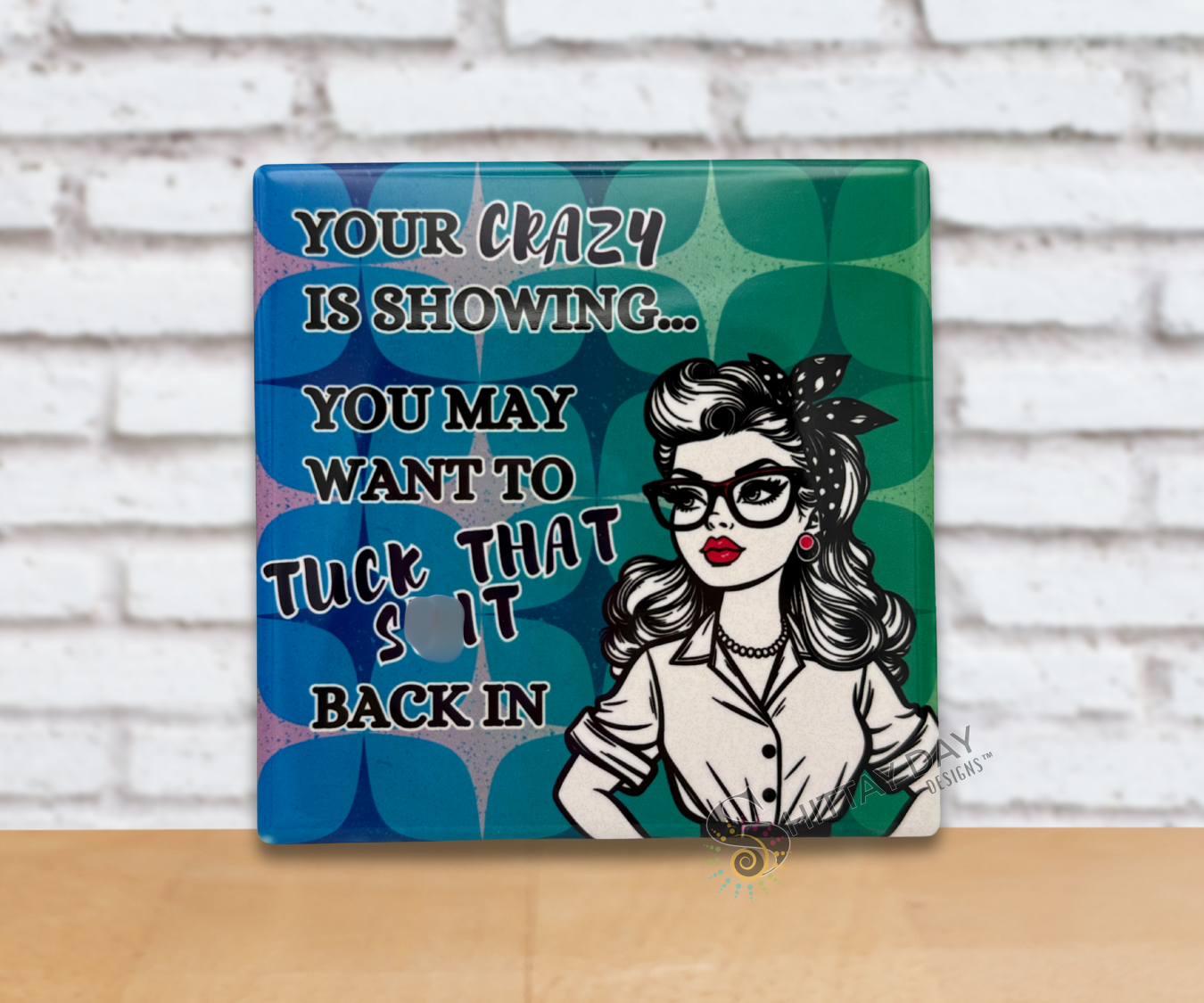 Retro vibe ceramic coaster upright with a woman's illustration and humorous text reading 'Your Crazy Is Showing, You May Want To Tuck That Shit Back in" on a blue and green patterned background.